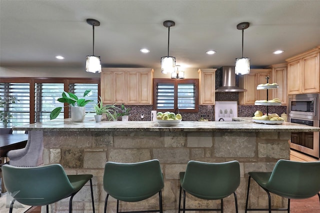 kitchen featuring stainless steel appliances, a wealth of natural light, hanging light fixtures, and wall chimney range hood