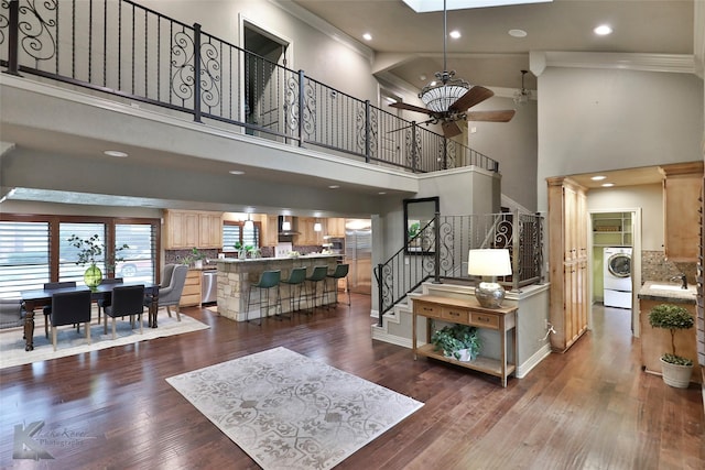 living room with ceiling fan, washer / dryer, dark wood-type flooring, and a high ceiling