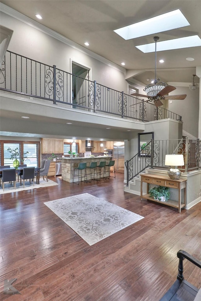 living room featuring hardwood / wood-style floors, a skylight, ornamental molding, and a high ceiling