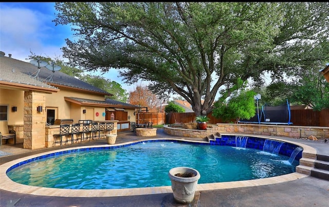 view of pool with an outdoor bar, a trampoline, pool water feature, area for grilling, and a patio