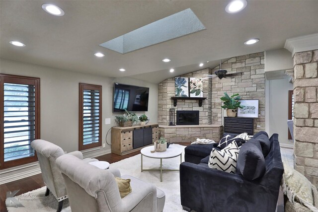 living room with hardwood / wood-style floors, ceiling fan, a stone fireplace, and a skylight