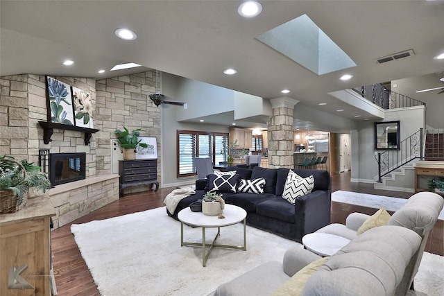 living room featuring ceiling fan, a stone fireplace, dark wood-type flooring, and decorative columns