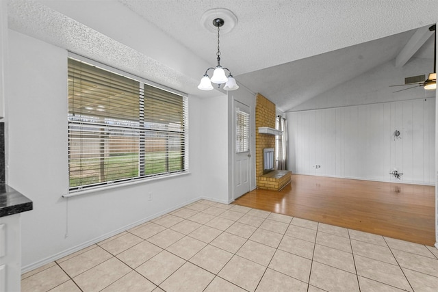 unfurnished dining area featuring ceiling fan with notable chandelier, a textured ceiling, vaulted ceiling, and light tile patterned flooring