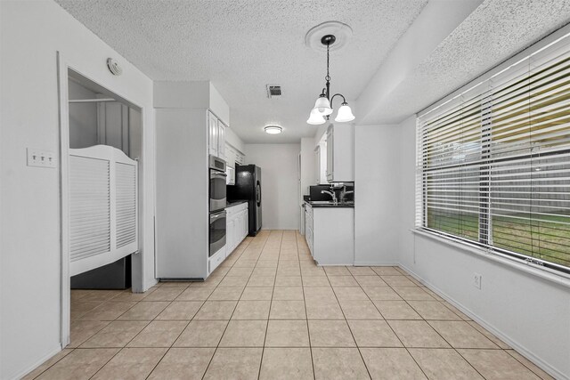 kitchen featuring double oven, sink, pendant lighting, a notable chandelier, and white cabinets