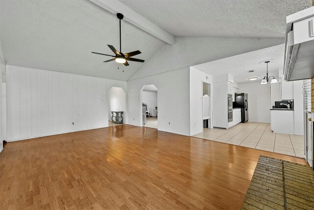 unfurnished living room with ceiling fan with notable chandelier, lofted ceiling with beams, a textured ceiling, and light wood-type flooring