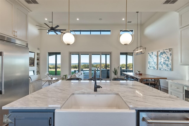 kitchen with stainless steel built in refrigerator, a high ceiling, sink, and an island with sink