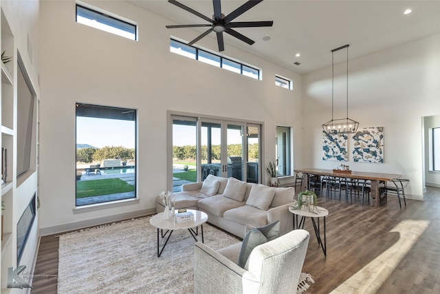 living room with french doors, ceiling fan with notable chandelier, dark wood-type flooring, and a high ceiling