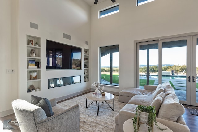 living room featuring french doors, a towering ceiling, built in shelves, ceiling fan, and hardwood / wood-style floors