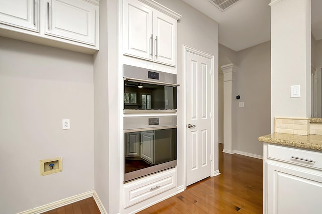 kitchen with visible vents, wood finished floors, light stone countertops, double oven, and white cabinetry