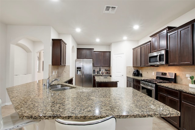 kitchen featuring sink, stainless steel appliances, dark stone counters, a breakfast bar, and a kitchen island