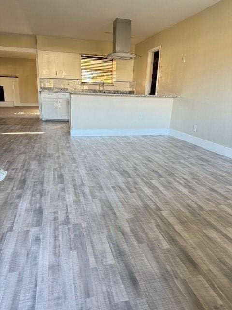 kitchen featuring sink, hardwood / wood-style flooring, wall chimney exhaust hood, light stone counters, and white cabinetry