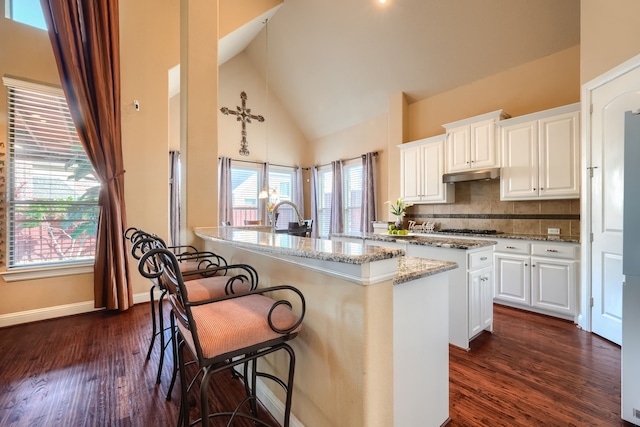 kitchen featuring pendant lighting, light stone countertops, white cabinets, and a center island with sink