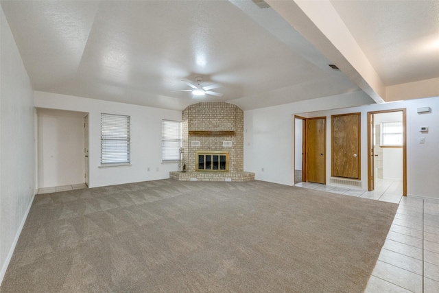 unfurnished living room with a brick fireplace, a textured ceiling, ceiling fan, light tile patterned floors, and lofted ceiling with beams