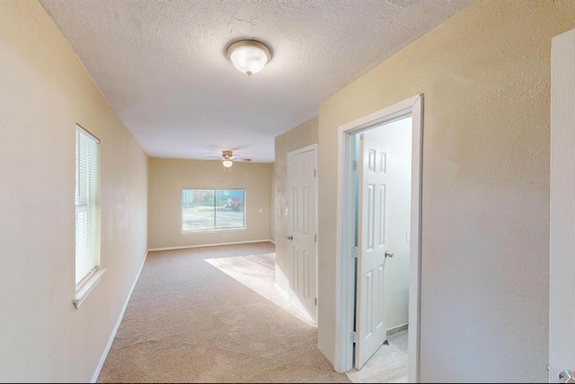 hall with light colored carpet and a textured ceiling