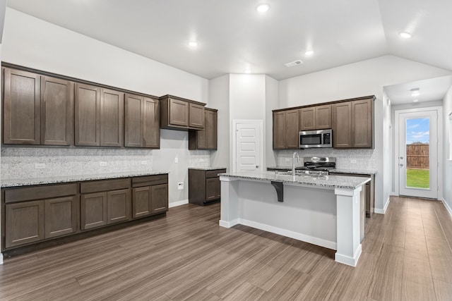 kitchen featuring dark hardwood / wood-style flooring, light stone countertops, appliances with stainless steel finishes, and tasteful backsplash