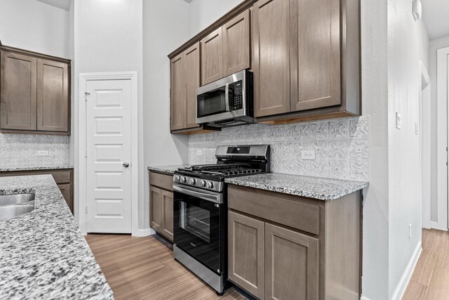 kitchen with decorative backsplash, light stone counters, stainless steel appliances, and light wood-type flooring