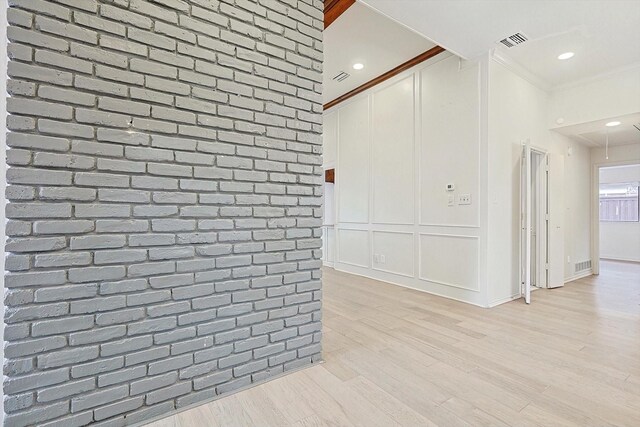 interior space with light hardwood / wood-style floors, brick wall, and ornamental molding