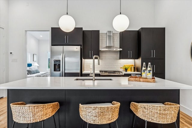 kitchen featuring hanging light fixtures, wall chimney exhaust hood, stainless steel appliances, and sink