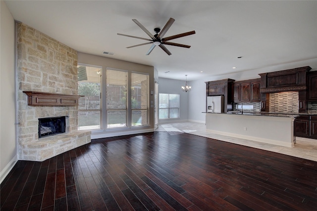 unfurnished living room featuring light wood finished floors, a stone fireplace, ceiling fan with notable chandelier, baseboards, and visible vents