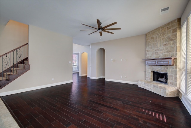 unfurnished living room with ceiling fan, arched walkways, a stone fireplace, wood finished floors, and visible vents