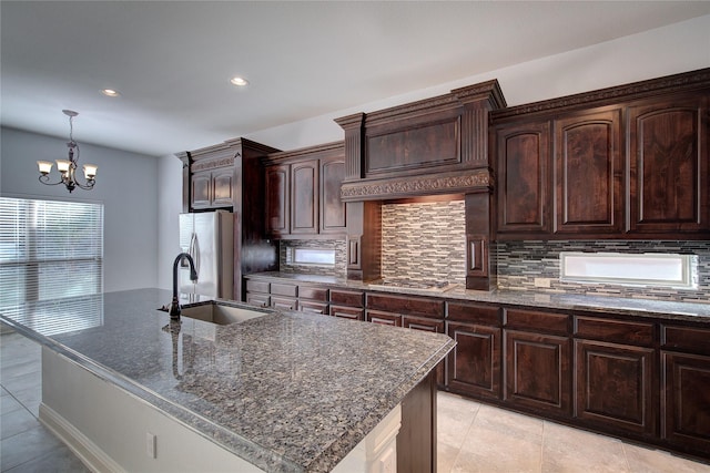 kitchen with a kitchen island with sink, sink, tasteful backsplash, dark brown cabinets, and a chandelier