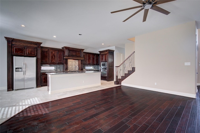 kitchen featuring ceiling fan, appliances with stainless steel finishes, a sink, a kitchen island with sink, and backsplash
