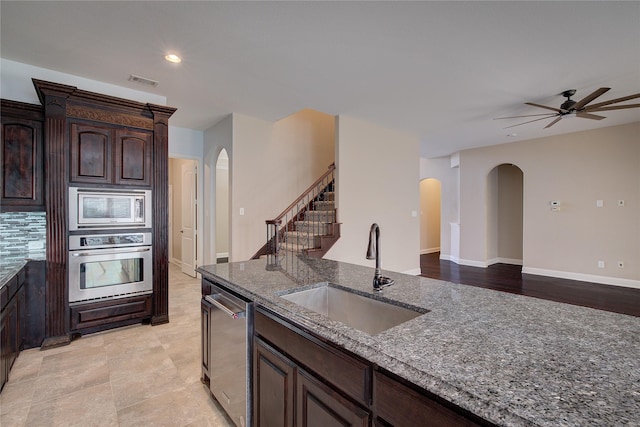 kitchen with appliances with stainless steel finishes, sink, dark stone countertops, ceiling fan, and dark brown cabinets