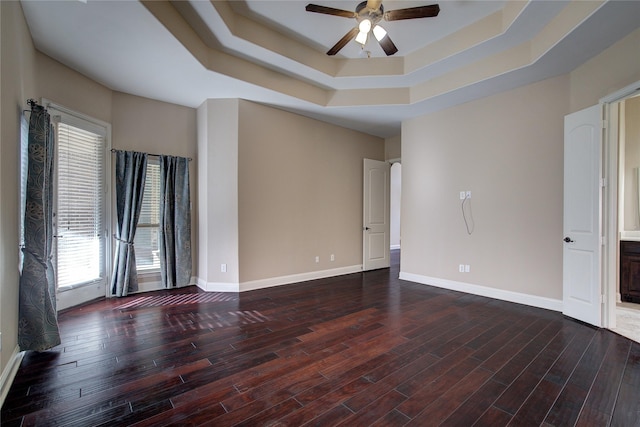 spare room featuring a raised ceiling, ceiling fan, and dark wood-type flooring