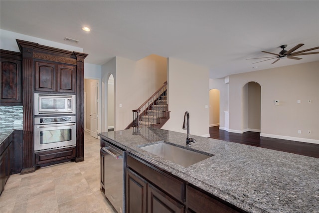 kitchen featuring visible vents, dark stone counters, arched walkways, a sink, and stainless steel appliances