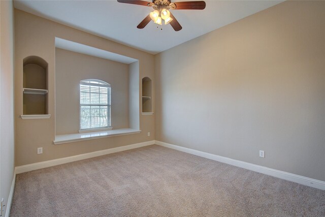 empty room with carpet floors, baseboards, built in shelves, and ceiling fan