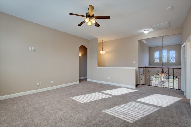 empty room featuring carpet flooring, arched walkways, a ceiling fan, baseboards, and visible vents