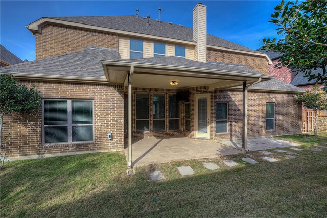 back of property with a lawn, a patio, roof with shingles, and brick siding