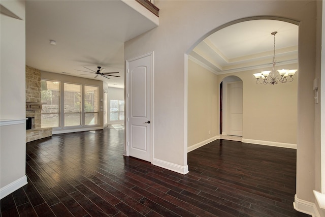 empty room featuring dark hardwood / wood-style floors, a stone fireplace, ornamental molding, and ceiling fan with notable chandelier