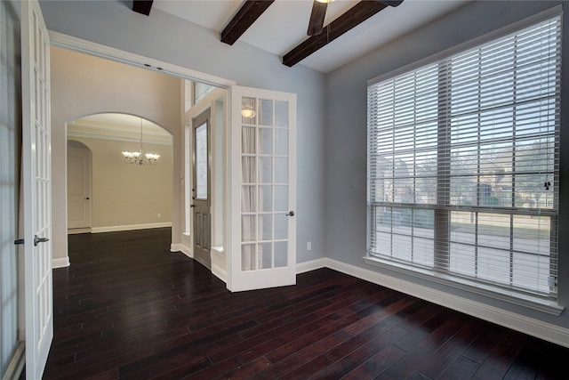 spare room with arched walkways, beamed ceiling, dark wood finished floors, and baseboards