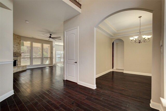unfurnished room with arched walkways, a stone fireplace, ceiling fan with notable chandelier, baseboards, and wood finished floors