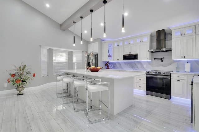 kitchen with a center island, hanging light fixtures, wall chimney range hood, white cabinets, and appliances with stainless steel finishes