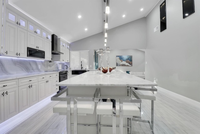 kitchen featuring stainless steel electric range, hanging light fixtures, wall chimney exhaust hood, a large island, and white cabinetry