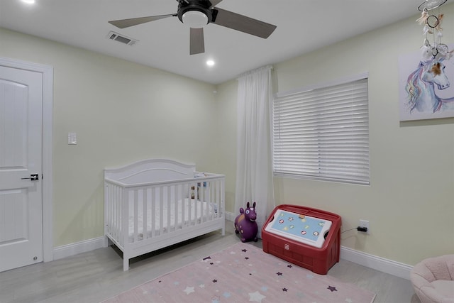 bedroom featuring ceiling fan, light wood-type flooring, and a nursery area