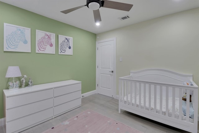 bedroom featuring ceiling fan, a crib, and light wood-type flooring