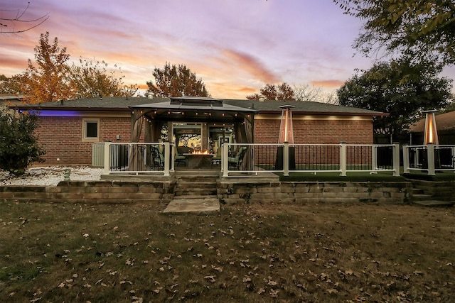 back house at dusk featuring a gazebo and a lawn