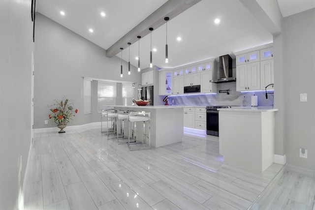 kitchen featuring pendant lighting, white cabinets, wall chimney exhaust hood, a kitchen island, and stainless steel appliances