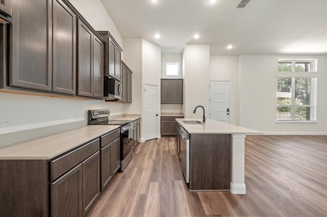 kitchen featuring hardwood / wood-style floors, a center island with sink, sink, appliances with stainless steel finishes, and dark brown cabinets