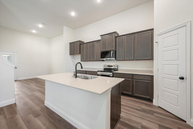 kitchen featuring sink, appliances with stainless steel finishes, dark brown cabinetry, a center island with sink, and dark hardwood / wood-style flooring