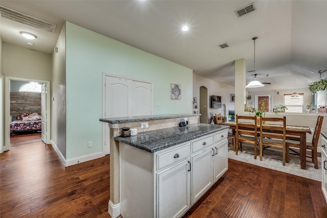 kitchen featuring dark wood-type flooring, decorative light fixtures, dark stone countertops, a kitchen island, and white cabinets