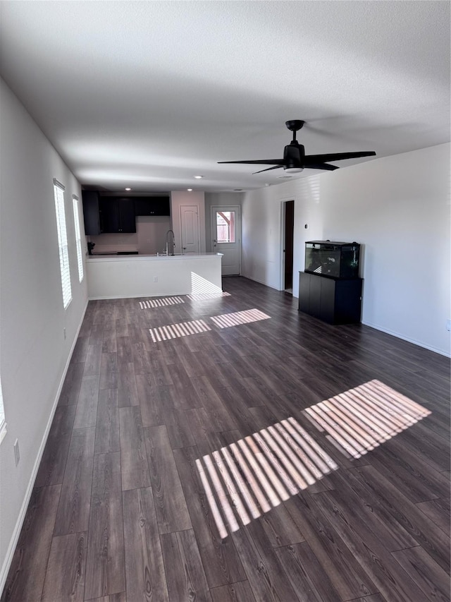 unfurnished living room featuring ceiling fan, sink, and dark wood-type flooring