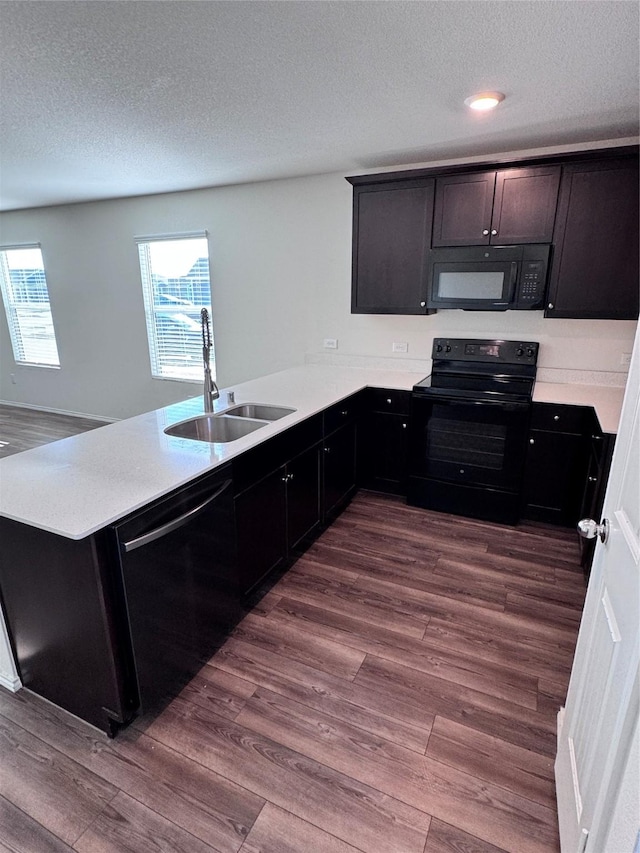 kitchen with hardwood / wood-style floors, kitchen peninsula, sink, and black appliances