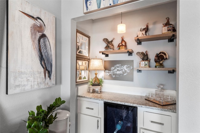 bar featuring white cabinetry, light stone counters, pendant lighting, and beverage cooler