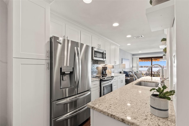 kitchen featuring sink, appliances with stainless steel finishes, white cabinetry, backsplash, and light stone countertops