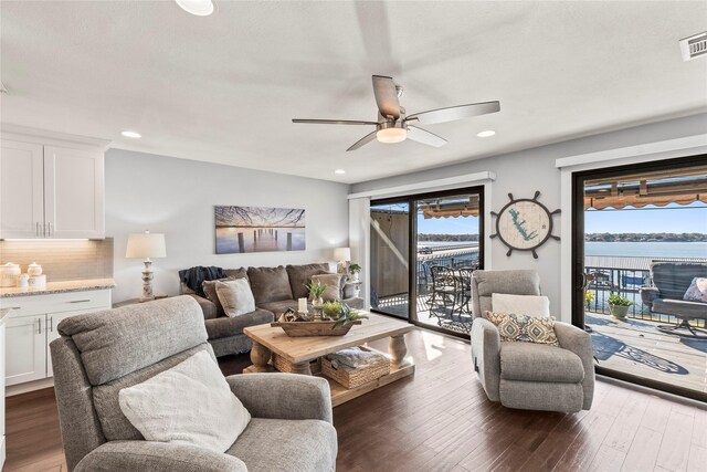 living room featuring ceiling fan, a water view, a healthy amount of sunlight, and dark hardwood / wood-style flooring