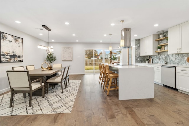 kitchen with white cabinets, hanging light fixtures, stainless steel dishwasher, and island range hood